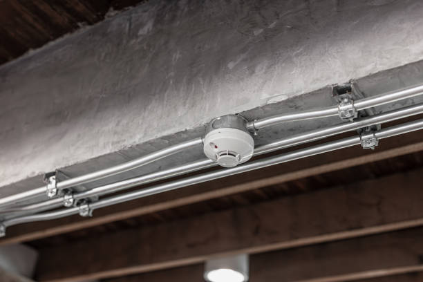 Detector de humo instalado en techo industrial con conducciones metálicas y estructura ignifugada