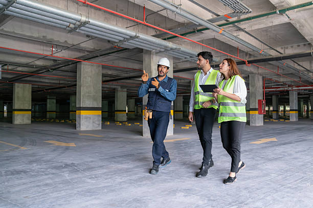 Técnico y responsables de obra inspeccionando instalaciones y tuberías en aparcamiento subterráneo vacío
